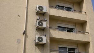 שלוש מרפסות בבניין מגורים בישראל עם מעבה מזגן ליד כל אחת, יונים מקננות על היחידות ולשלשת על הקיר